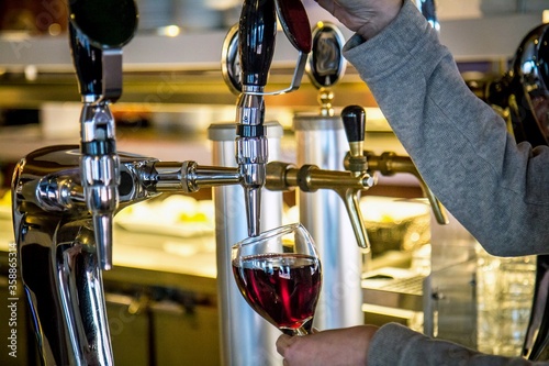Unidentified man is pouring red wine into a glass from tap at buffet lunch.