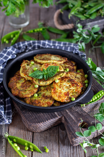 Zucchini fritters with herbs in frying pan on a wooden table. Healthy food