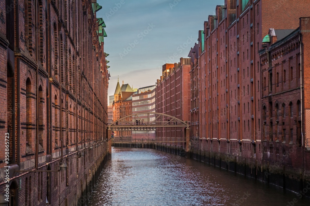 Canal in Hamburg, Germany, and pedestrian bridge across it. The Speicherstadt, the largest warehouse district in the world where the buildings stand on timber-pile foundations, oak logs.