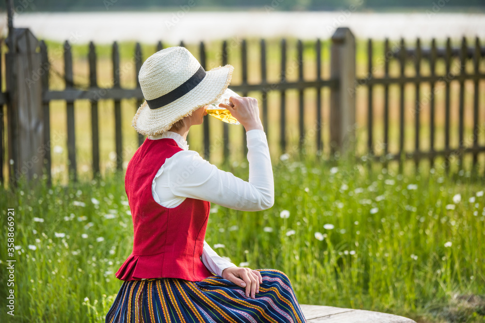 Fototapeta premium Woman drinking beer on a bench. Ligo folk.