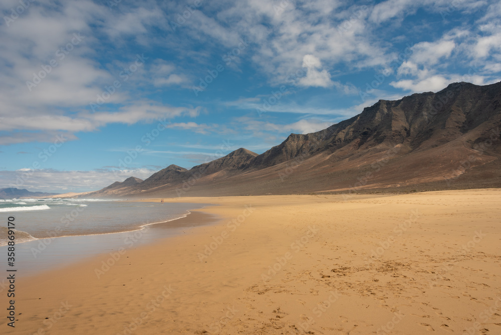 Famous Cofete beach, Fuerteventura Island. Yellow sand under blue sky. High mountains in the background. 