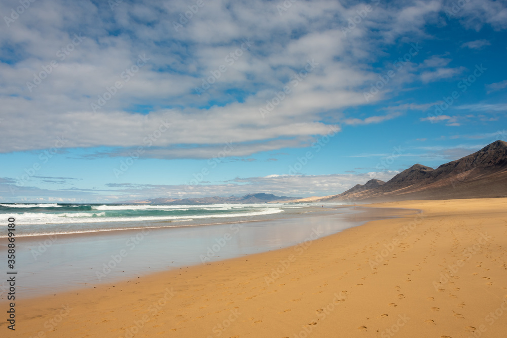 Famous Cofete beach, Fuerteventura Island. Yellow sand under blue sky. High mountains in the background. Famous Cofete beach, Fuerteventura Island. Yellow sand under blue sky. High mountains in the background.