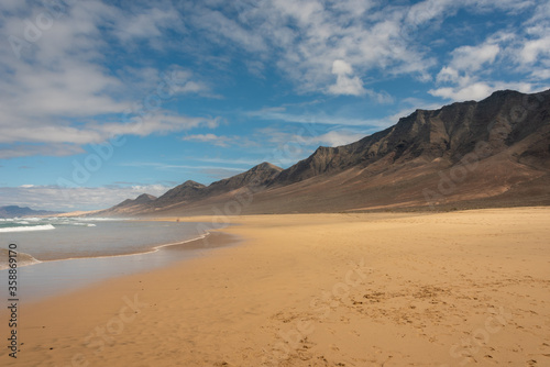 Famous Cofete beach, Fuerteventura Island. Yellow sand under blue sky. High mountains in the background. 
