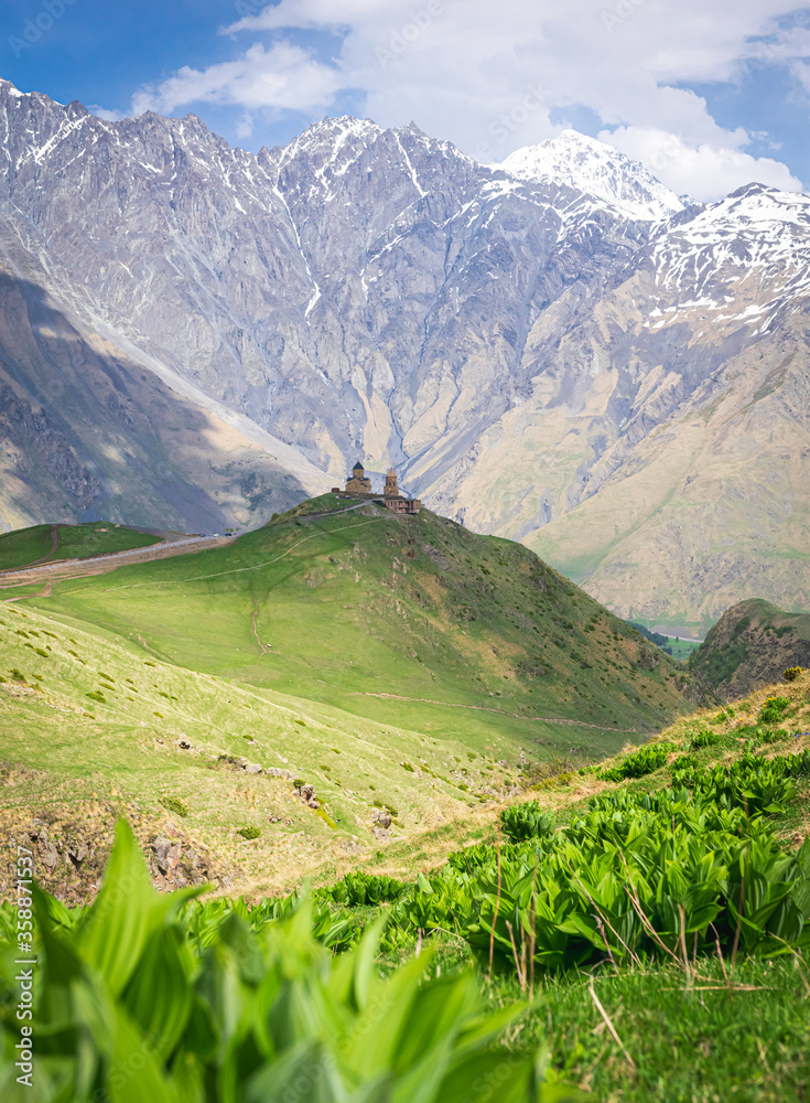 Obraz premium Historical Gergeti trinity church on top of the hill surounded by green nature and mountain in the background. Travelous in KAzbegi national park. Sakartvelo