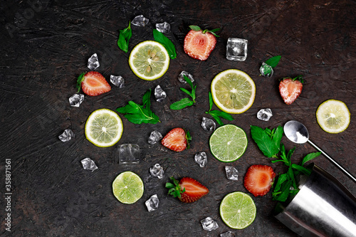 Creative summer cocktail drink composition with strawberries, lemon slices, ice cubes, mint leaves and bar tool on dark background.