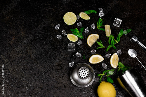 popular alcohol drink summer cocktail mojito creative composition with lemon slices, ice cubes, mint leaves and bar tool on dark background