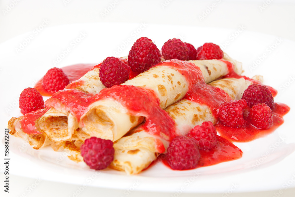 Thin pancakes twisted into a roll with sauce, decorated with raspberries Thin pancakes twisted into a roll with sauce, decorated with raspberries