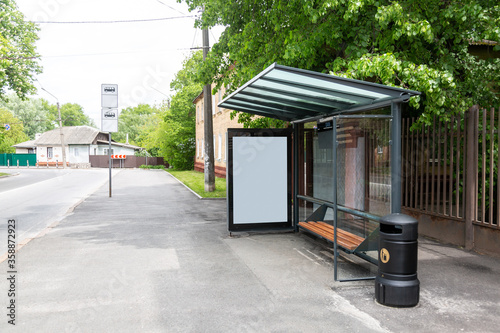 Public transport stop in the city with an empty place for an advertising poster banner. Near trees and houses. Horizontal orientation. 