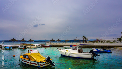 Fishing boats waiting on seaport or harbor. Small boats on Aegean sea under cloudy sky. Luxury yachtes / anchored boats waiting on coast or seaside. Richness and wealth concept. Copy space for text.