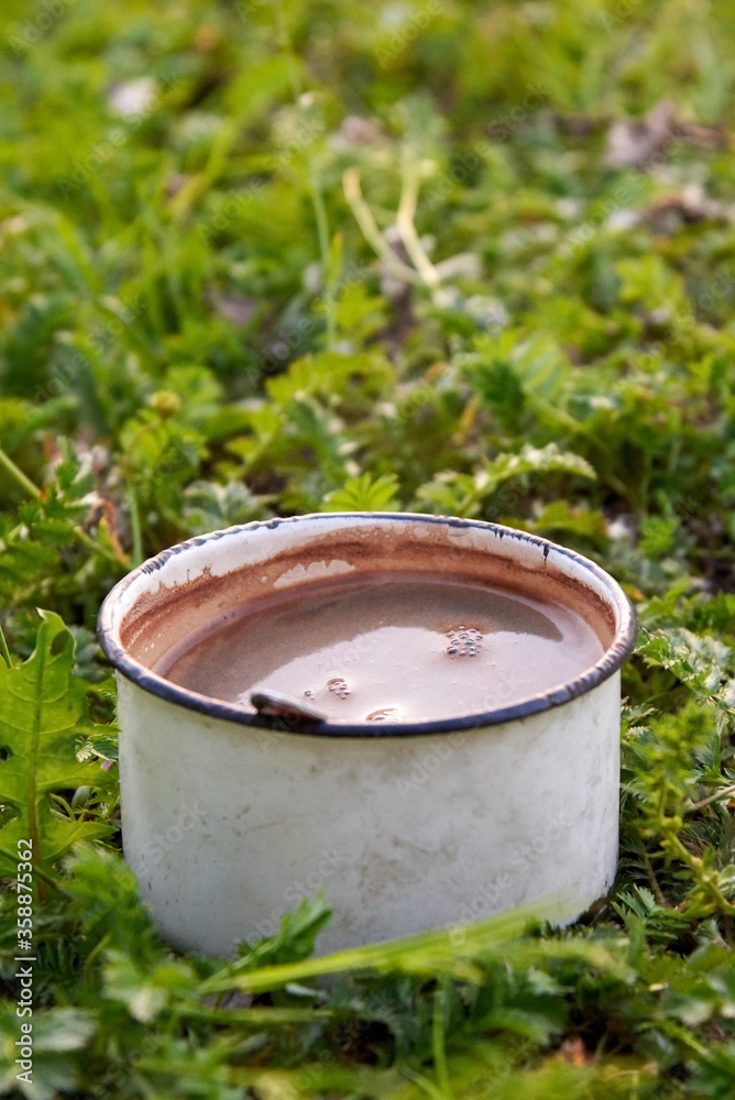 Old metal mug with coffee on the grass.