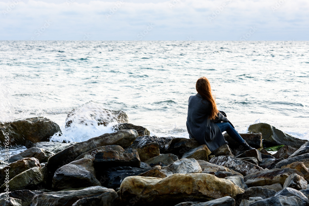 A girl sits on stony stones by the sea and looks into the distance A girl sits on stony stones by the sea and looks into the distance