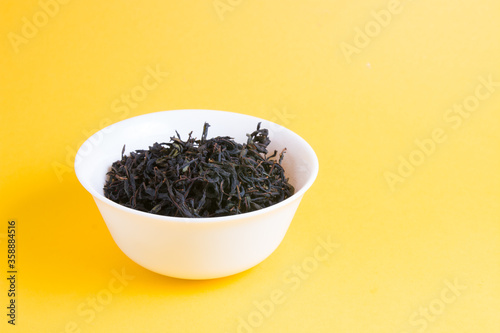 mixed black tea in little white bowl on a yellow background, copy space