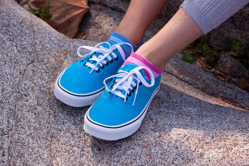 Girl's legs with turquoise sneakers resting on speckled rock