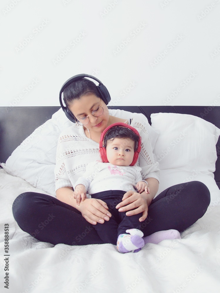 Joven madre y su pequeña hija sentadas en la cama con auriculares ...
