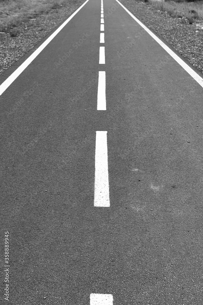 Perspective road marked with white dotted lines. grass along the way. black and white image.