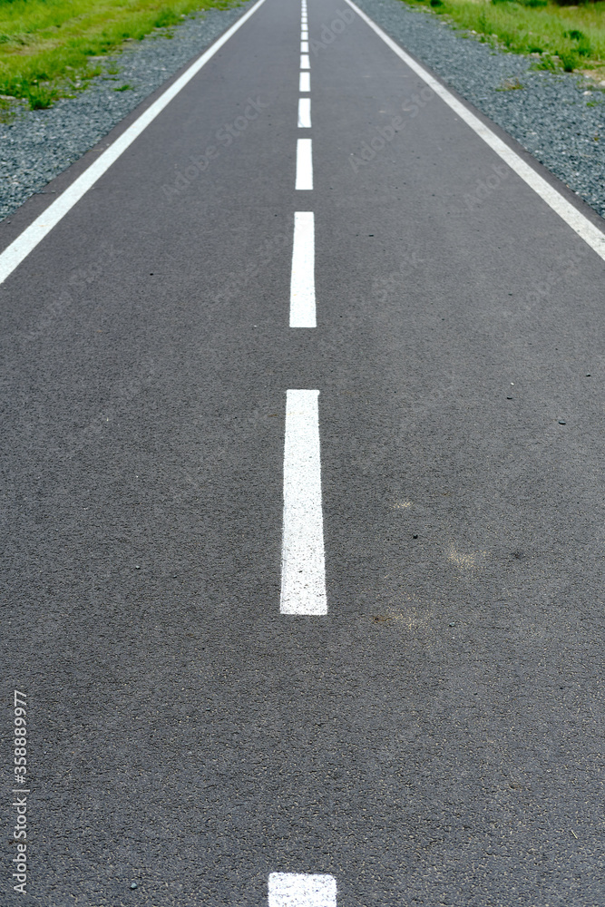 Perspective road marked with white dotted lines. Green grass along the way.