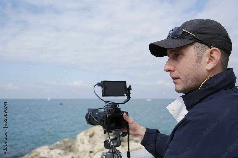 Obraz premium portrait videographer or photographer or blogger with digital camera and screen in action on a sea