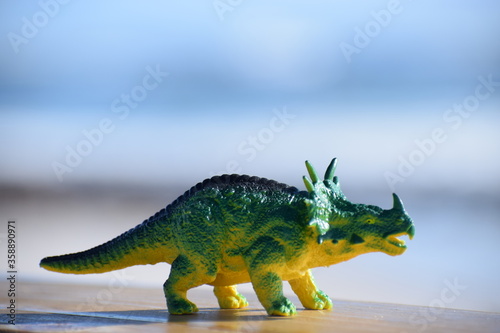 Fototapeta Naklejka Na Ścianę i Meble -  Dinosaur toy standing outside with the beach and ocean in the background.