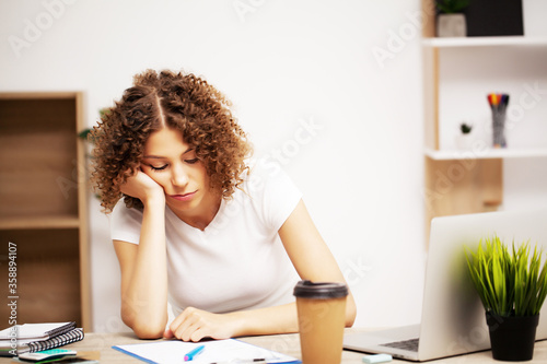 Tired woman with curls on her head working in the office on a laptop