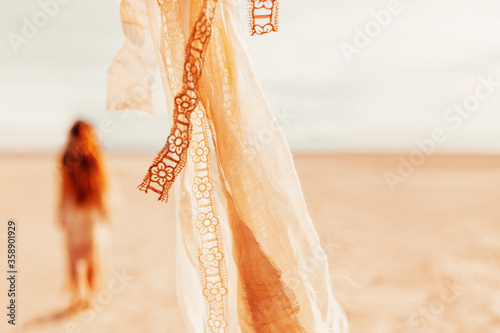 close up of beige fabric and lace foreground and young beatiful woman at background on the beach at sunset