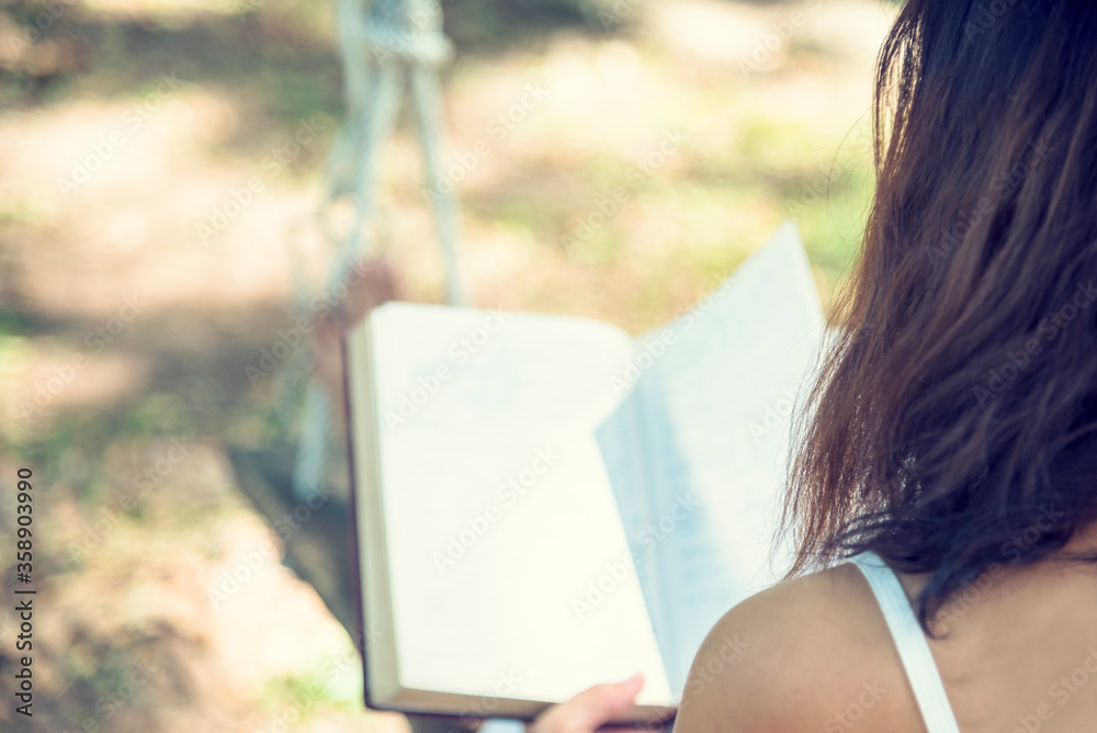 Obraz premium Relax woman holgind bible book read outdoors sitting on green garden in park. Young woman relaxation reading open book in autumn fall season at home garden. Smart beautiful woman lifestyle learner.