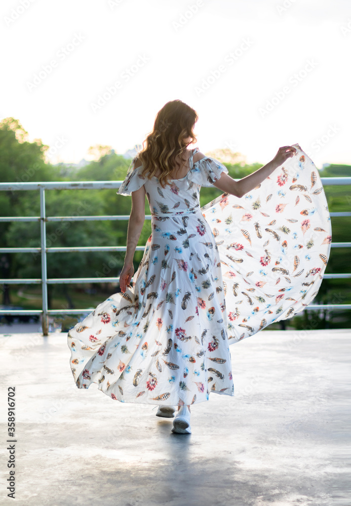 girl dancing in white dress on the terrasse, keeps the dresses edges