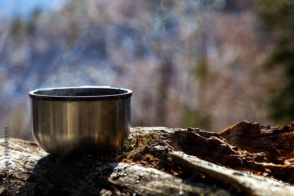 Thermos metal mug with tea on a background of wildlife