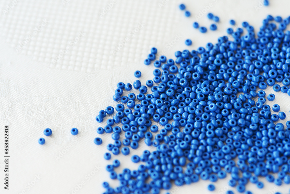 Seed beads blue color scattered on a textile background close-up. Handmade, art, creativity Seed beads blue color scattered on a textile background close-up. Handmade, art, creativity