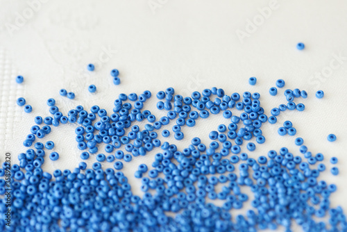 Seed beads blue color scattered on a textile background close-up. Handmade, art, creativity