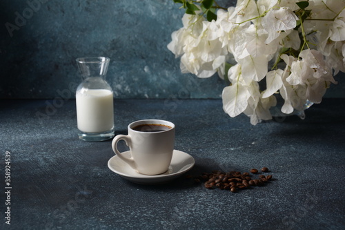 Composition with white cup of coffee   beans  and flowers as background