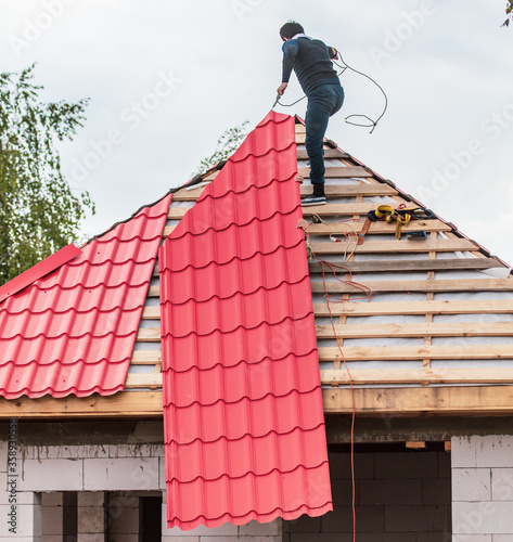 Workers install red metal tiles on the roof