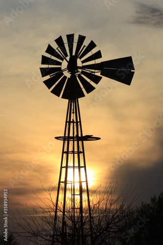 Kansas Country Windmill at Sunset with clouds and tree's north of Hutchinson Kansas USA.