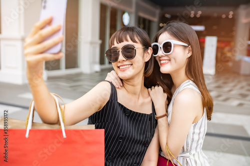 Attractive beautiful asian friends women using smartphone. Happy woman with shopping .urban city while taking self portraits with friends together. Girl holding colour bag.Friends walking in mall.