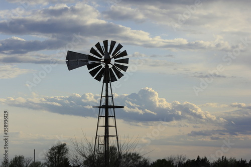 Kansas Country Windmill at Sunset with clouds and tree's north of Hutchinson Kansas USA.