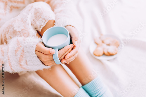 Young woman on the bed with with cup of milk in hands enjoys her stay at home.