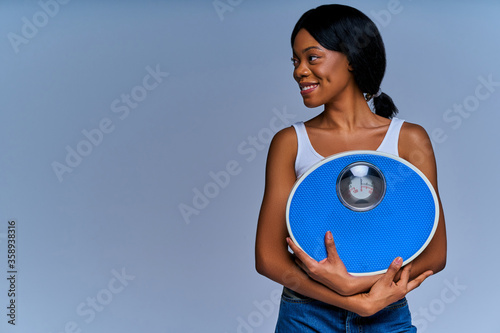 Slim smiling girl in white top and jeans has weighing-machine thinking . Diet concept
