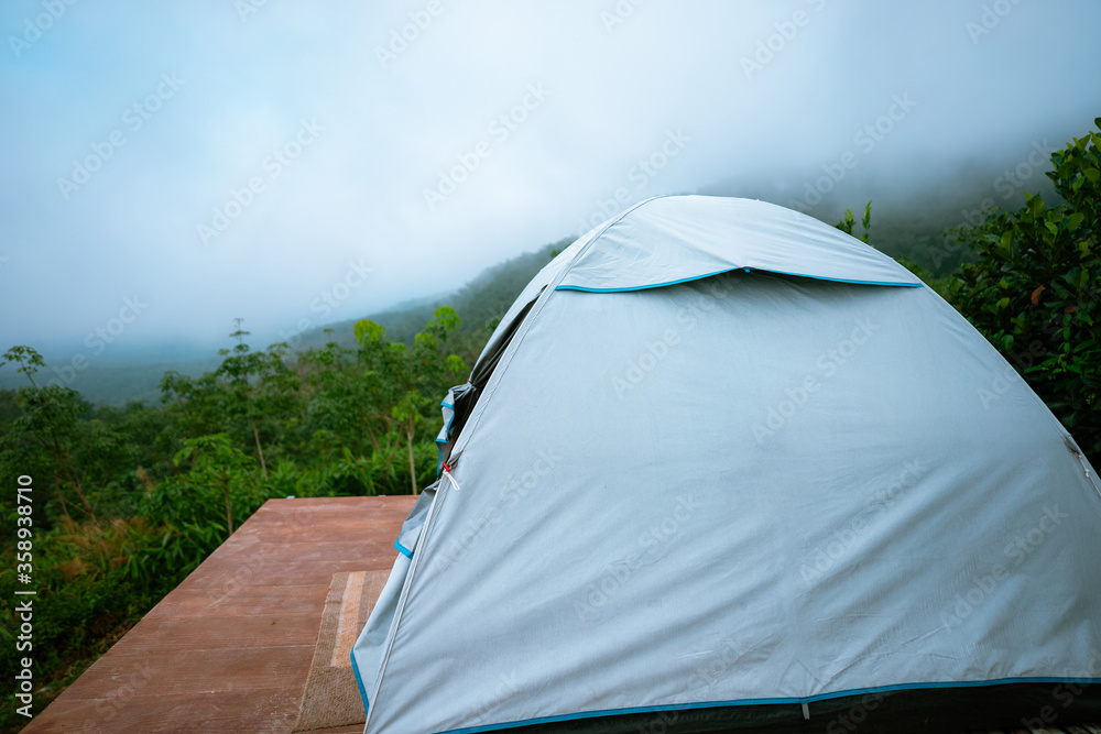 white tent on wooden platform in the middle of the forest with view of mountain, green trees and fog.