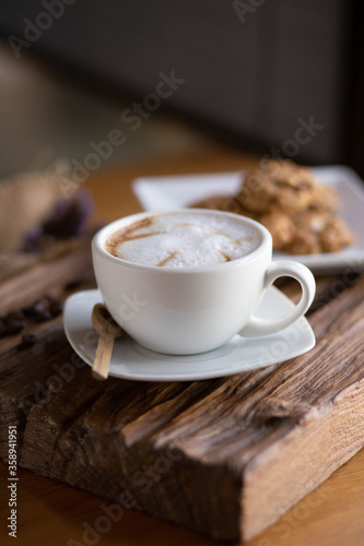 Cappuccino coffee on wood in the morning with cookies on dish at cafe,selective focus.