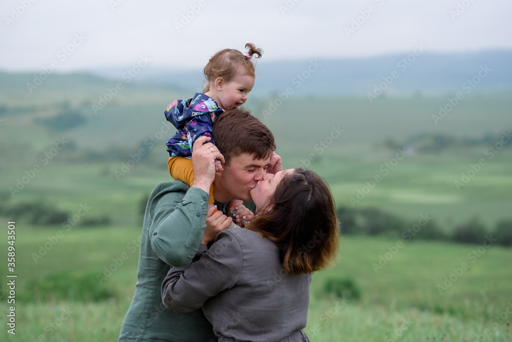 Mom, dad and daughter. Daughter is sitting on the neck of his father. Parents are kissing. Close-up. Mom, dad and daughter. Daughter is sitting on the neck of his father. Parents are kissing. Close-up.