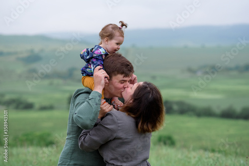 Mom, dad and daughter. Daughter is sitting on the neck of his father. Parents are kissing. Close-up. © wolfhound911