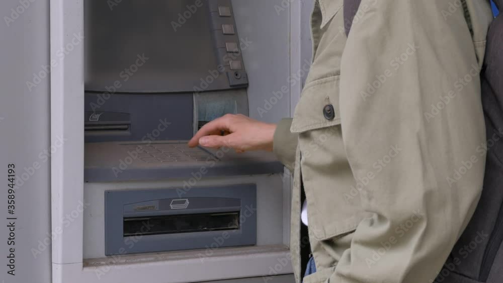 A woman's hand pressing buttons, entering a pin code into a damaged ATM.