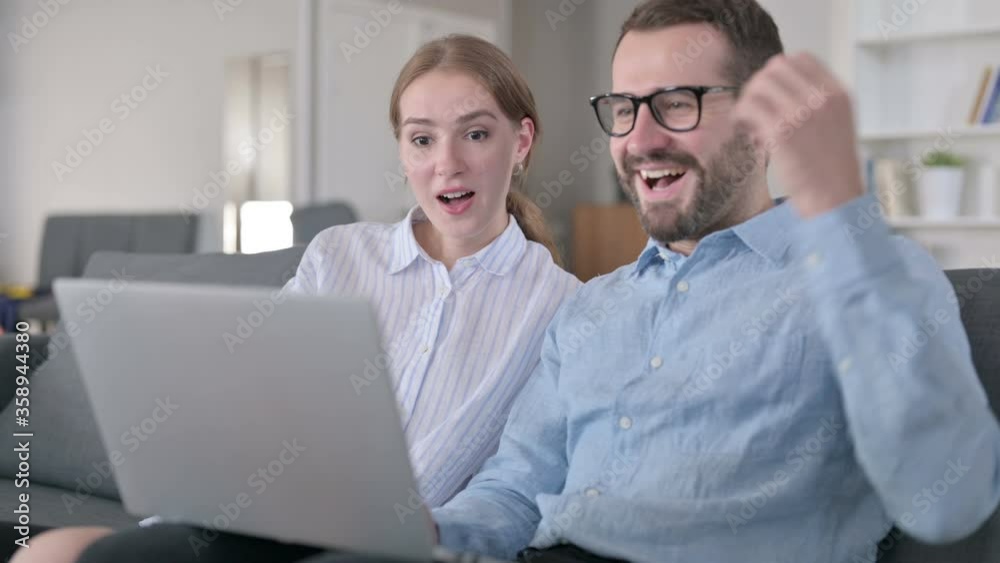 Excited Young Couple Celebrating Success on Laptop at Home 