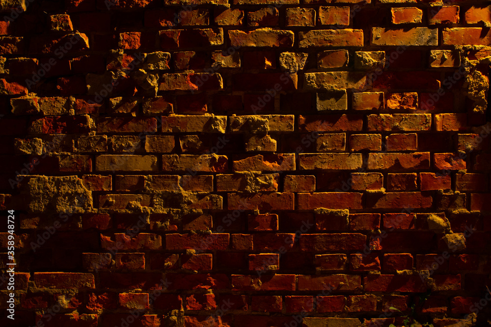 Old grungy and damaged red brick wall at night with light of a lantern shining on it