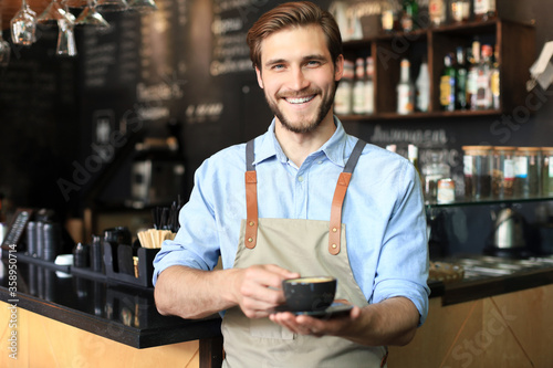 Handsome barista offering a cup of coffee to camera at the coffee shop. photo
