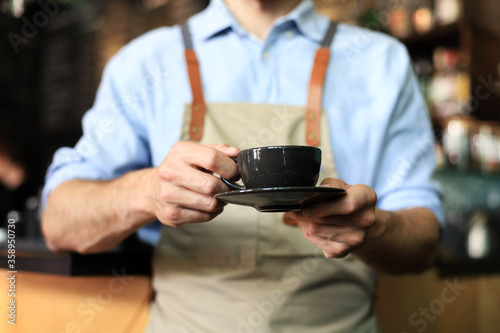 Barista offering a cup of coffee to camera at the coffee shop.