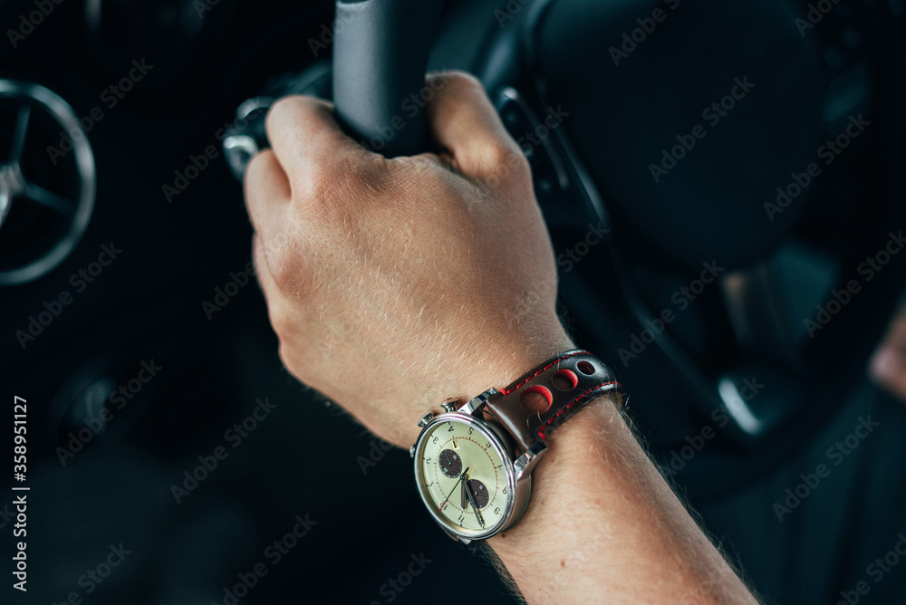 male hand with a clock holds the steering wheel of a car