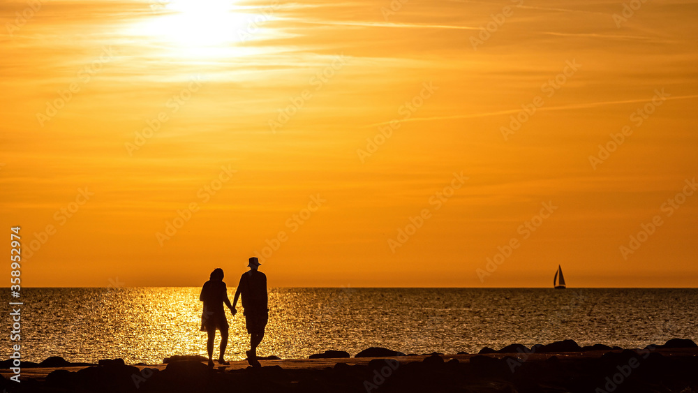 silhouette of couple walking on the pier during the golden hour of sunset