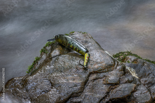 Colorful fishing hook, plummet and baits for catching fish on wet rock background. Long exposure of silky smooth water. Fishing and hobbies concepts, close up photo