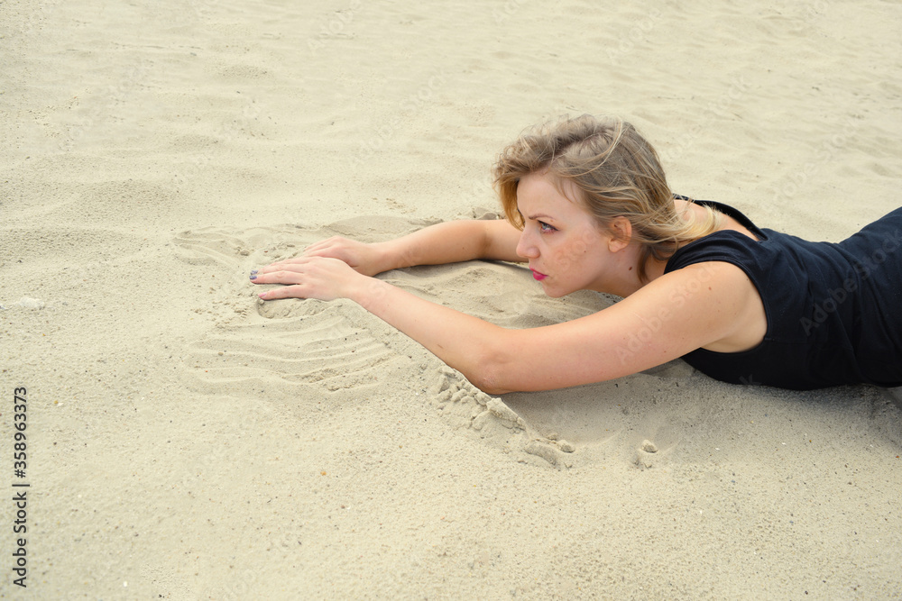 Young woman in a black swimsuit is lying on the sand in the desert Young woman in a black swimsuit is lying on the sand in the desert