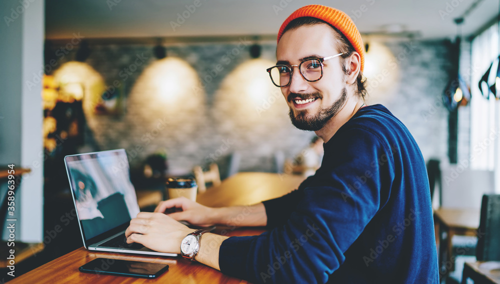 Portrait of happy male freelancer in optical eyewear smiling at camera during break from working online, positive cheerful hipster blogger sitting on publicity area with modern laptop computer Portrait of happy male freelancer in optical eyewear smiling at camera during break from working online, positive cheerful hipster blogger sitting on publicity area with modern laptop computer